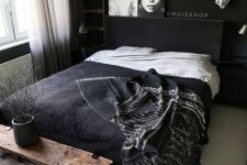 a contemporary moody bedroom with black walls, black furniture and a wooden bench, pendant lamps and art