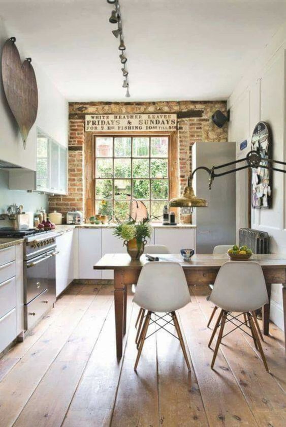 a cottage kitchen with white cabinetry, stone countertops, a brick wall, metal appliances and a vintage wooden table and white chairs