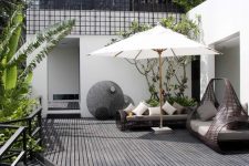 a modern black deck with dark rattan furniture, neutral textiles, a large umbrella and lots of greenery