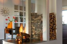a modern white fireplace with a glass cover and firewoo storage is a nice space divider and is a very cozying up piece