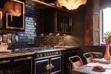 a moody and glam kitchen with black cabinetry, metallic patterns, a black tile backsplash, a pendant lamp, a rough table and leather chairs
