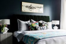 a moody bedroom with navy walls and a ceiling, a dark green velvet bed, a glam gold chandelier and striped nightstands