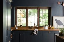a moody kitchen wiht black cabinetry, wooden countertops, wooden frames and beams, metallic handles and an artwork