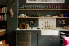 a moody kitchen with graphite grey cabinets, white marble countertops, shelves, molding and dark furniture plus an artwork