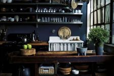 a moody kitchen with navy walls, dark cabinetry, a rough wooden kitchen island, metal shelves and a holder with pans
