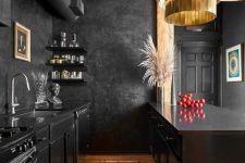 a moody yet bold kitchen with black cabinetry, black walls, a wooden ceiling, a gold chandelier and pampas grass in a vase