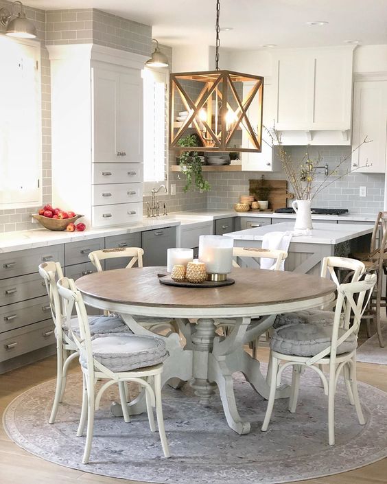 a neutral farmhouse kitchen with grey and white cabinetry, a pendant lamp, a large round wooden table and chairs