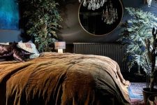 a refined vintage moody bedroom with dark walls, a black radiator, a crystal chandelier, potted plants and dark bedding