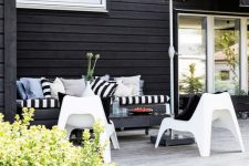 a small modern deck with a black bench, white chairs, a black table on casters and a black umbrella