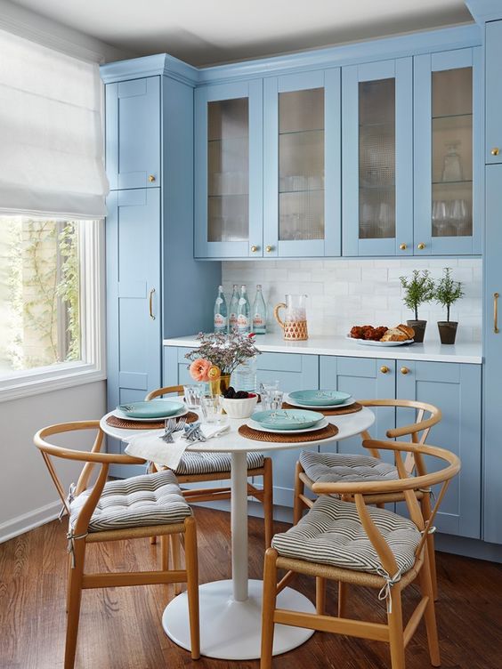 a stylish blue kitchen with a white tile backsplash and a dining zone with a round table and wooden chairs with striped cushions