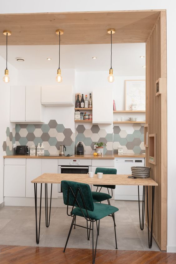 a stylish contemporary kitchen in white, with grey, green and neutral hex tiles, green chairs and a small hairpin leg table