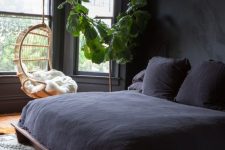 a stylsh modern moody bedroom in black, with a pendant chair, a dark wooden bed and a cool chandelier, a statemtn plant in a pot