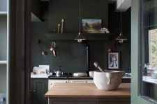 a vintage moody kitchen in dark green and lighter shades of green, a grey kitchen island with a wooden countertop and pendant lamps