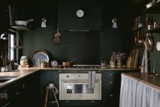 a vintage moody kitchen with black walls and cabinetry, wooden countertops, lamps and a kitchen island with a curtain