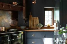 a vintage moody kitchen with graphite grey cabinetry, a black hearth and wooden countertops plus wooden beams on the ceiling