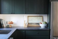a vintage moody kitchen with sleek dark cabinetry, a grey stone countertop, a white tile backsplash and some art
