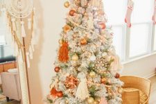 02 a lovely flocked Christmas tree with pastel boho decor, orange, gold and blush ornaments, beadsm large tassels and lights