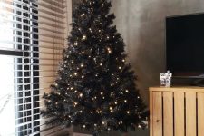 05 a black Christmas tree with only lights and pillows covering the base is a lovely and minimal idea for a modern space