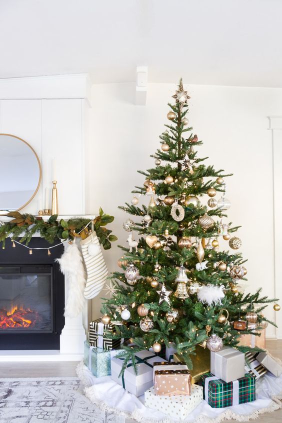 a glam Christmas tree with gold and white ornaments, lights and piles of gifts under it is lovely and chic