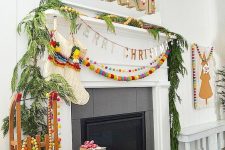 13 a colorful and fun boho Christmas fireplace and mantel with fir branches, colorful pompoms and a large sign with letters