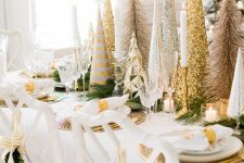 19 a glam Christmas tablescape done with gold chargers and an arrangement of shiny metallic trees, with gold candleholders and napkin rings and all white everything