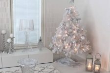 19 a white and silver living room with a white Christmas tree with lights and silver ornaments, white snowflakes hanging from the ceiling and shiny pillows