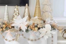 24 glam and chic Christmas mantel decor with snowflake stockings, gold and white flower garlands, leaves and an arrangement of Christmas trees