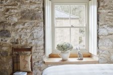 a French farmhouse bedroom with a stone accent wall, vintage furniture and shabby wooden beams that add charm here