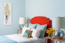 a beautiful bedroom with light blue walls, a red upholstered bed, printed and pastel bedding, wooden nightstands and silver table lamps