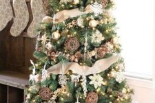 a beautiful rustic Christmas tree with lights, burlap ribbons, vine balls, snowflakes and pinecones and a bucket