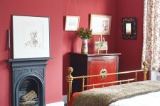 a beautiful vintage bedroom with red walls, a gold bed, a redwood dresser, chic artworks and a built-in fireplace