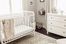 a beautiful vintage nursery in neutrals, with white furniture, white textiles, a chair, layered rugs and some artworks