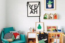 a bold and chic nursery with colorful bedding, toys, artworks, accessories, a turquoise chair and bright house-shaped shelves