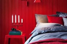 a bold modern bedroom with a red accent wall,grey, red and burgundy bedding, a red nightstand and a catchy candelabra is a wow space