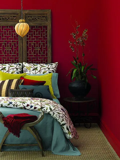 a bold red bedroom with a unique carved wooden screen as a headboard, printed bedding, a beautiful pendant lamp and some greenery in a pot