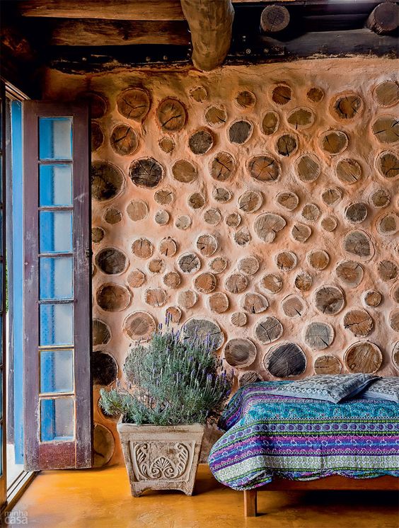 a bright boho space with a terracotta and wood slice accent wall, simple furniture and bright textiles plus a statement plant