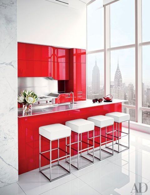 a bright minimalist red and white kitchen with sleek metal backsplashes and countertops and a row of white stools