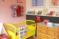 a bright nursery with a pink printed wall, a color block wall, a yellow crib, a bold patchwork rug, lots of colorful books and artworks