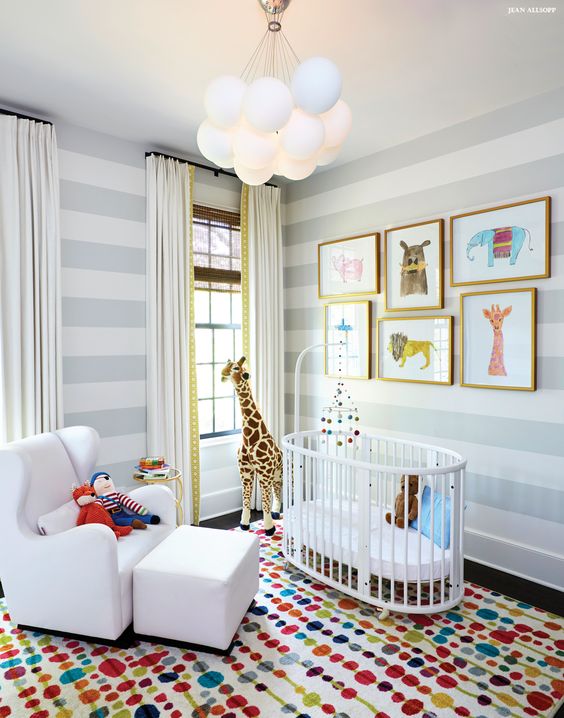 a bright nursery with striped walls, a super colorful rug, neutral textiles, a fun and bright gallery wall with framed art