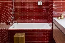 a bright red bathroom clad with subway tiles, with a floatign wooden vanity, white appliances, a wooden stool and a boho rug
