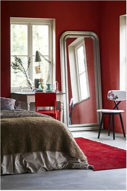 a bright red bedroom with neutral vintage furniture, an oversized mirror, a red chair and a floral one, a red rug is super bold