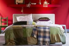 a bright red eclectic bedorom with a shelf over the bed, a white bed with printed bedding, accessories and decor and a pendant lamp