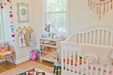 a cheerful nursery done in neutrals, with a mirror dresser, colorful bedding, rugs and garlands is very fun
