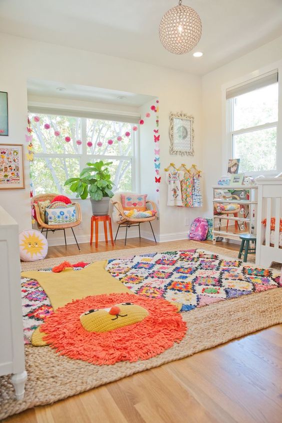 a cheerful nursery with bold layered rugs, garlands, pillows, bedding and neutral furniture and a mirror dresser