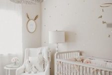 a chic and cozy white nursery with a heart wall, white vintage furniture, a beaded chandelier and a mobile and a mirror