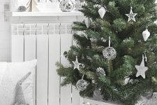 a chic modern Christmas tree with white and silver ornaments of creative shapes, in a white basket and with lights is cool