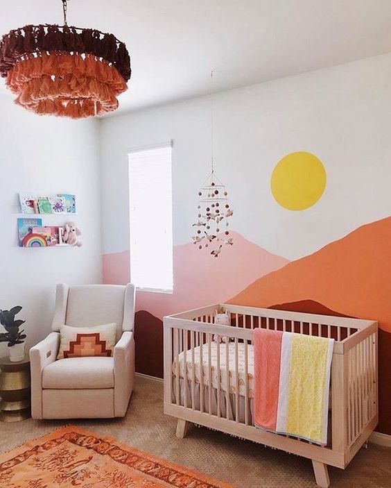 a colorful nursery with bold mountains painted, colorful bedding and rugs, a bold ombre tassel chandelier and bright books