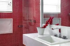 a contemporary bathroom with a red tile shower space, a wood and marble vanity, a large mirror and some leaves