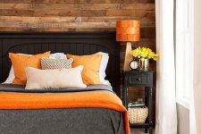 a cozy bedroom with a reclaimed wooden wall and bold orange accents that add a cheerful touch to the space