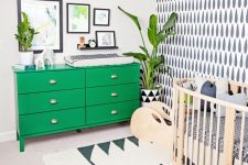 a fun nursery done in black and white, with lots of graphic patterns, a bold green dresser and an ottoman, statement plants and artworks